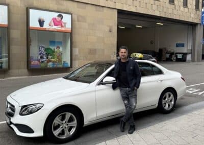 Weißes Mercedes-Benz E-Klasse Taxi mit Spezialumbau für den Rollstuhltransport, inklusive Rampe und Sicherungssystem für sitzende Beförderung.